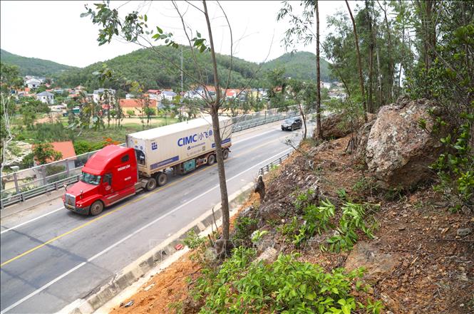 Phương tiện cơ giới lưu thông qua đoạn đường có nguy cơ sạt lở đất, đá lăn ở khu vực đầu cầu Lạch Quèn. Ảnh: Xuân Tiến - TTXVN 

