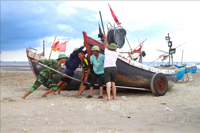 Ngư dân làng biển hợp sức đẩy thuyền mủng từ trên cạn xuống nước. Ảnh: Xuân Tiến - TTXVN 