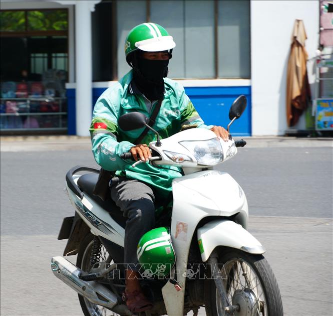 Lái xe công nghệ mặc đồ bảo hộ chống nắng nóng gay gắt khi di chuyển trên đường Trần Hưng Đạo, phường Phú Xuân, thành phố Huế. Ảnh: Nguyên Lý - TTXVN