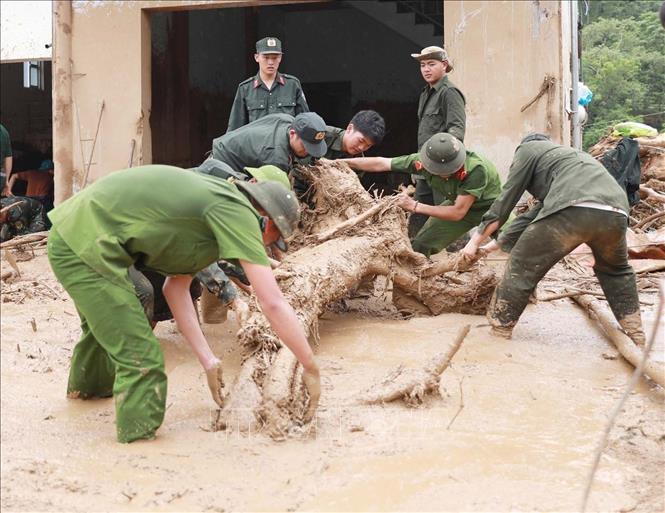 Lực lượng Công an giúp dân dọn bùn đất, đá, cây gỗ trôi vào nhà tại xã Mường Than. Ảnh: Quý Trung - TTXVN