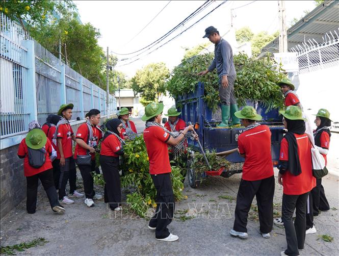 Đội hình sinh viên tình nguyện Malaysia tham gia thu gom cành cây, vệ sinh môi trường tại phường Trung Mỹ Tây. Ảnh: Trung Tuyến - TTXVN