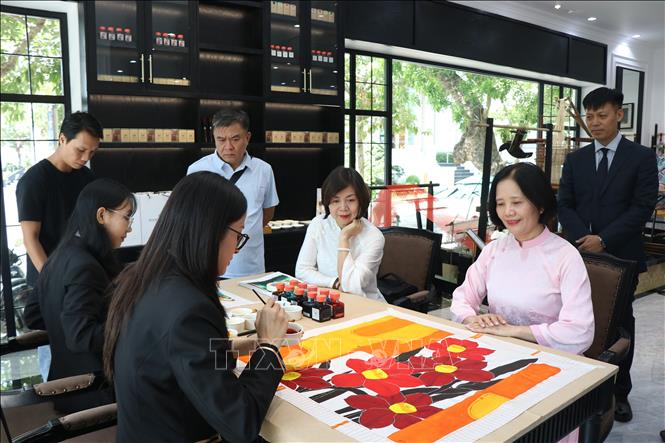 Du khách được chiêm ngưỡng quá trình thiết kế và vẽ hoạ tiết lên các chiếc khăn được làm từ tơ lụa truyền thống. Ảnh: Mai Trang- TTXVN 
