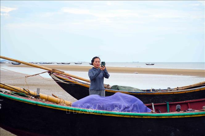 Bà Nguyễn Thị Thanh Hương ghi lại khoảnh khắc những con thuyền cập bến sau chuyến vươn khơi. Ảnh: Hữu Quyết - TTXVN