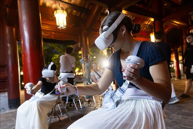 Du khách nước ngoài sử dụng thiết bị thực tế ảo để khám phá không gian văn hóa di sản trong tour đêm. Ứng dụng kính thực tế ảo (VR) vào bảo tồn di sản là điểm nhấn đột phá, giúp các tour du lịch đêm của Hà Nội trở nên hấp dẫn du khách, hiện đại nhưng vẫn đậm đà bản sắc. Ảnh: Tiến Long/TTXVN phát
