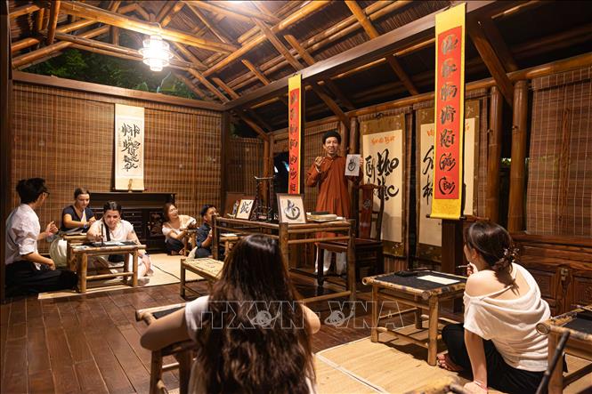 Du khách trong và ngoài nước trải nghiệm lớp học thư pháp cùng thầy đồ tại không gian nhà thầy đồ thuộc tour trải nghiệm đêm “Tinh hoa đạo học” - Văn Miếu - Quốc Tử Giám. Việc đưa các hoạt động tương tác văn hóa dân gian vào chương trình du lịch ban đêm giúp đa dạng hóa sản phẩm, gia tăng trải nghiệm thực tế và quảng bá giá trị di sản Thủ đô tới khách du lịch. Ảnh: Tiến Long/TTXVN phát
