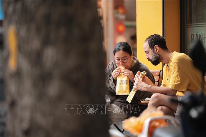 Tourists have a taste of banh mi in Hanoi. VNA Photo