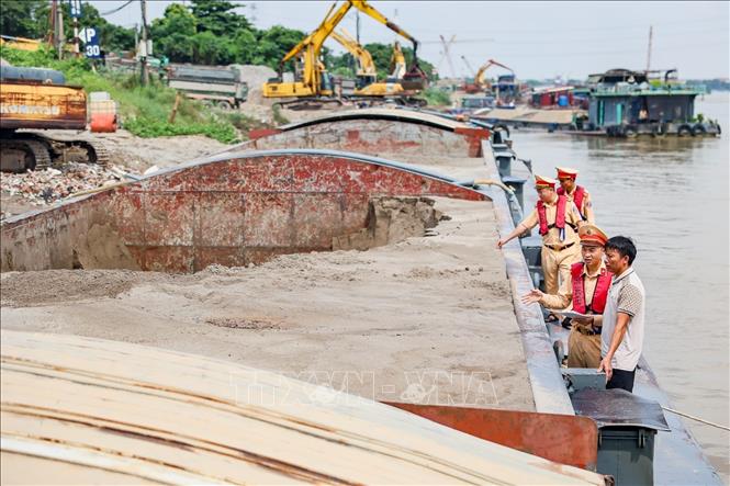 Lực lượng Đội Cảnh sát đường thủy số 2 kiểm tra phương tiện vận chuyển vật liệu đang neo đậu tại một bến, bãi ven sông Hồng. Ảnh: Trung Nguyên - TTXVN