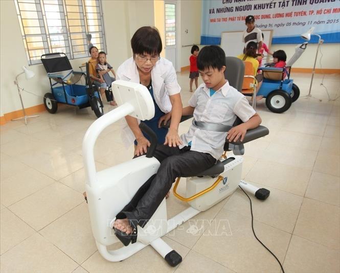 Nhân viên Trung tâm Nuôi dưỡng, phục hồi chức năng và dạy nghề cho nạn nhân chất độc da cam tại thành phố Đông Hà, tỉnh Quảng Trị giúp trẻ em là nạn nhân chất độc da cam/dioxin tập phục hồi chức năng (2015). Ảnh: Anh Tuấn - TTXVN