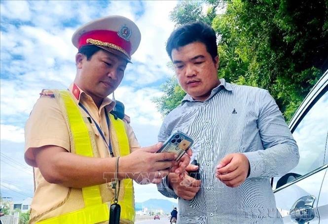 Cán bộ, chiến sĩ Trạm CSGT Tuy Phước, Phòng CSGT Công an tỉnh Bình Định hướng dẫn người dân tích hợp giấy phép lái xe, giấy tờ xe trên ứng dụng VneID (26/07/2024). Ảnh: Lê Phước Ngọc - TTXVN