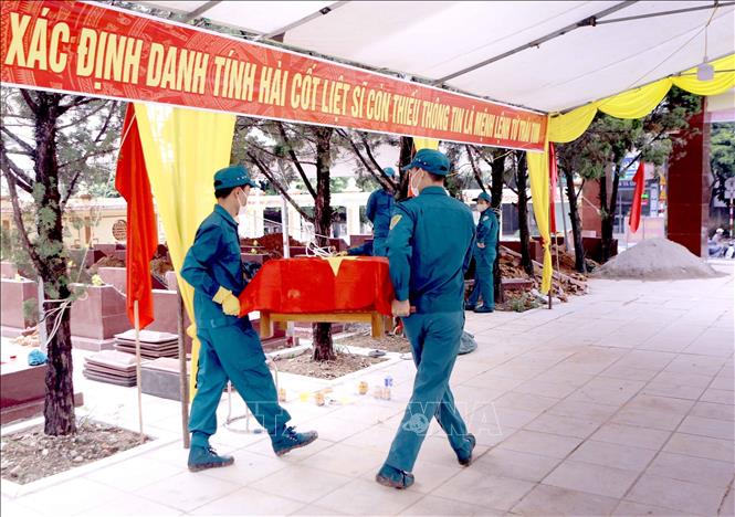 Lực lượng chức năng đưa tiểu sành chứa hài cốt liệt sĩ trở lại phần mộ sau khi hoàn thành lấy mẫu tại Nghĩa trang liệt sĩ Hợp Lý, xã Hợp Lý. Ảnh: Hoàng Hùng - TTXVN