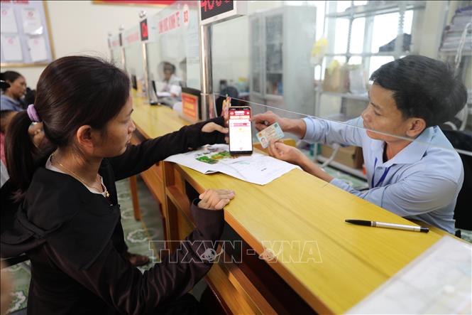 Cán bộ Trung tâm Phục vụ hành chính công xã Đồng Tiến hướng dẫn người dân cài đặt, sử dụng các ứng dụng trên điện thoại thông minh để thực hiện thủ tục hành chính. Ảnh: Khiếu Tư - TTXVN
