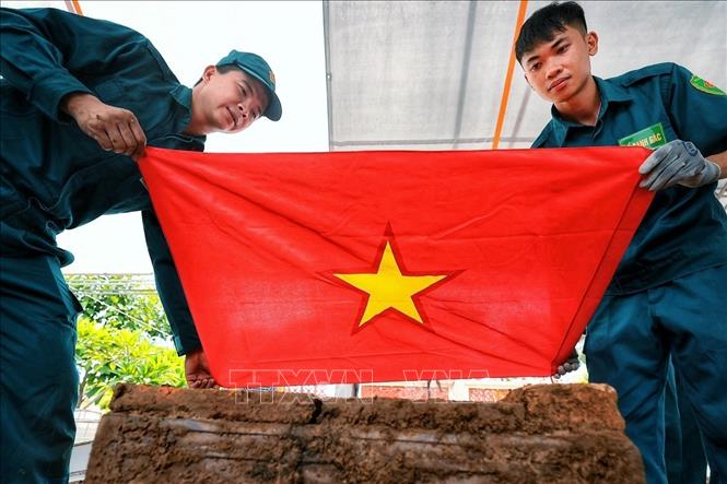 Các thành viên tổ công tác trang trọng phủ Quốc kỳ lên phần hài cốt liệt sĩ sau khi được đưa lên khỏi vị trí an táng, trước khi chuyển đến khu vực chuyên môn để thực hiện các bước lấy mẫu phục vụ giám định ADN. Ảnh: Phạm Tuấn Anh - TTXVN