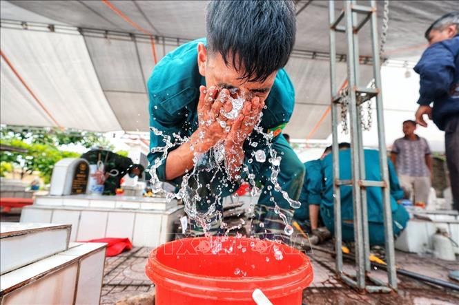 Chiến sĩ dân quân tự vệ tranh thủ rửa mặt sau thời gian làm việc liên tục dưới thời tiết nắng nóng tại khu vực mở mộ. Sau ít phút nghỉ ngắn, các lực lượng tiếp tục công việc, bảo đảm tiến độ nhiệm vụ lấy mẫu hài cốt liệt sĩ. Ảnh: Phạm Tuấn Anh - TTXVN