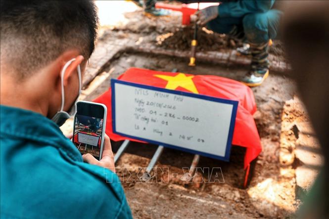 Các thành viên tổ số hoá chụp lại bảng thông tin, mã số và vị trí phần mộ nhằm bảo đảm dữ liệu được ghi nhận, đối chiếu chính xác trong suốt quá trình lấy mẫu hài cốt liệt sĩ. Ảnh: Phạm Tuấn Anh - TTXVN