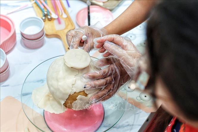 An artisan meticulously smooths and adjusts the outer dough layer of the mooncake to perfect the vase shape before decorating it and adding *tò he* (traditional dough figurine) flower pieces. VNA Photo: Phạm Tuấn Anh