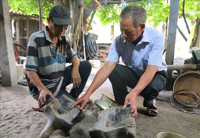 Ông Đỗ Đức Cảm (bìa trái) chia sẻ về quy trình sản xuất đồ đồng. Ảnh: Đinh Hương - TTXVN