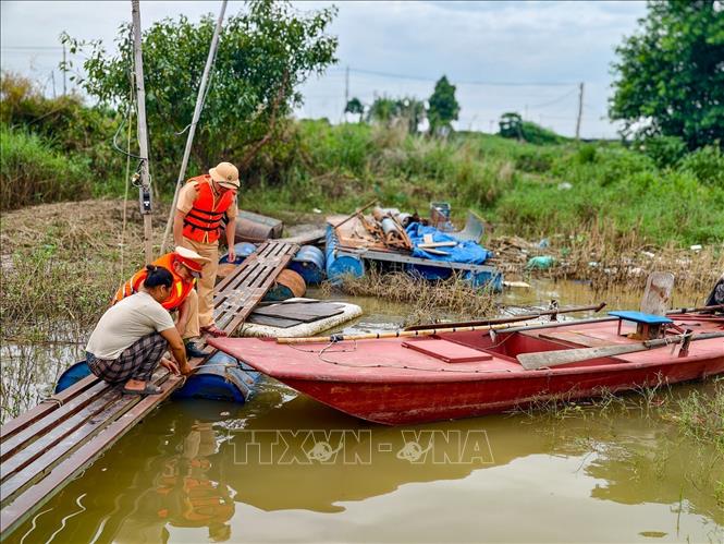 Cán bộ Đội Cảnh sát đường thủy số 2 hỗ trợ người dân kiểm tra dây neo, bảo đảm an toàn cho phương tiện khi nước sông dâng cao. Ảnh: Trung Nguyên - TTXVN