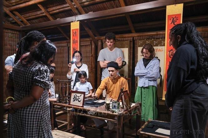Văn hóa được bảo tồn và phát huy. Trong ảnh: Du khách theo dõi nghệ nhân trình diễn thư pháp trong không gian văn hóa truyền thống tại tour đêm Văn Miếu. Ảnh: Phạm Tuấn Anh – TTXVN