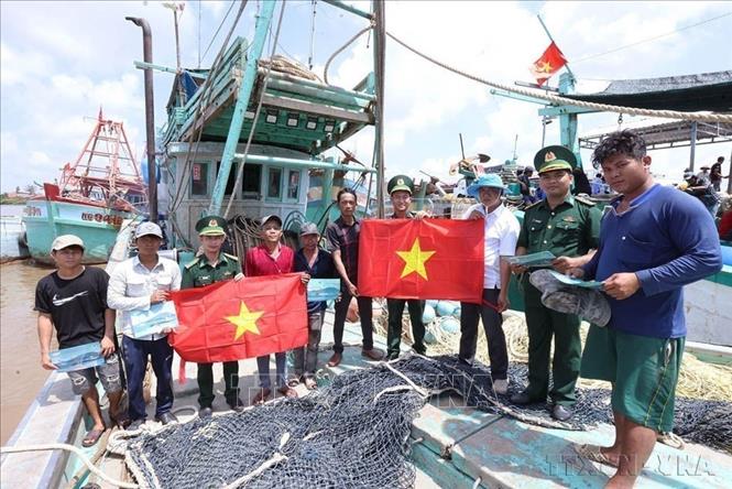 Bảo vệ biên giới, chủ quyền quốc gia gắn với giữ gìn an ninh và cuộc sống bình yên của nhân dân. Trong ảnh: Bộ đội Biên phòng đồn Cái Cùng, xã Vĩnh Hậu, tỉnh Cà Mau tuyên truyền vận động và tặng cờ Tổ quốc cho ngư dân trước khi ra khơi khai thác hải sản theo quy định (IUU). Ảnh: Vũ Sinh - TTXVN