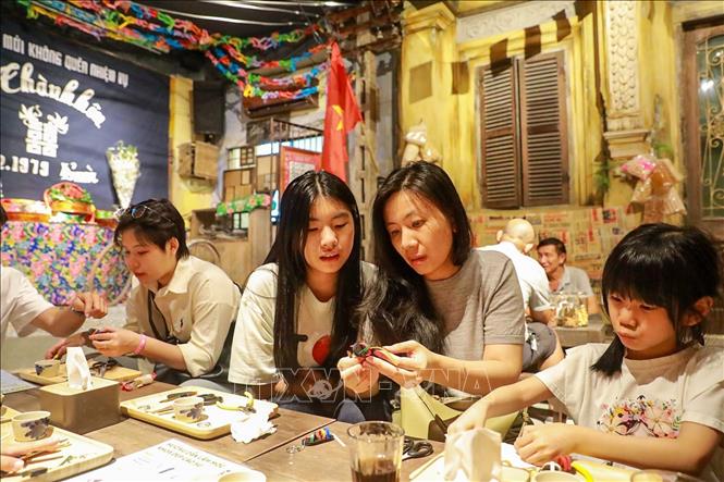 Khách tham quan trải nghiệm làm dép lốp. Ảnh: Khánh Hoà - TTXVN
