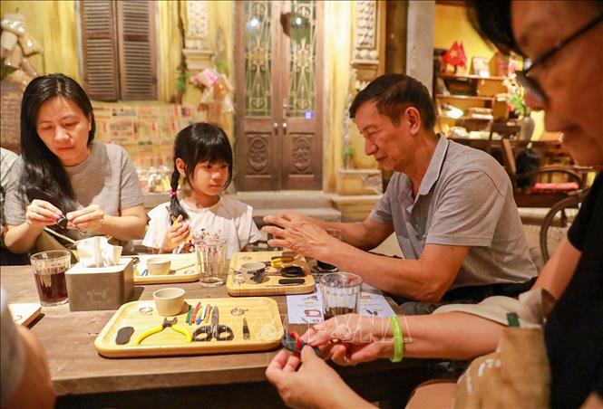 Khách tham quan trải nghiệm làm dép lốp. Ảnh: Khánh Hoà - TTXVN
