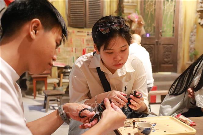 Khách tham quan trải nghiệm làm dép lốp. Ảnh: Khánh Hoà - TTXVN
