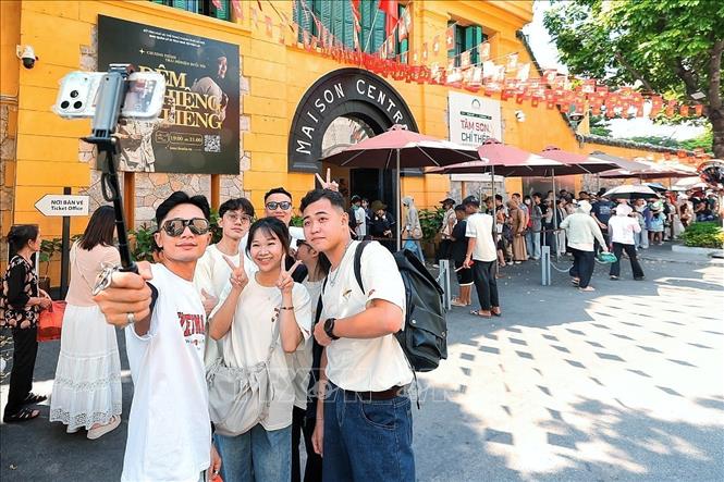 Nhiều bạn trẻ tranh thủ ghi lại khoảnh khắc bên Di tích Nhà tù Hỏa Lò trong khi phía sau, dòng khách vẫn nối dài chờ vào tham quan. Ảnh: Phạm Tuấn Anh - TTXVN