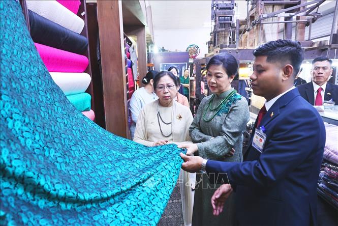 Phu nhân Ngô Phương Ly và Phu nhân Kyu Kyu Hla tham quan khu trưng bày sản phẩm lụa truyền thống và giới thiệu các sản phẩm đặc sắc của làng nghề. Ảnh: Minh Đức – TTXVN

