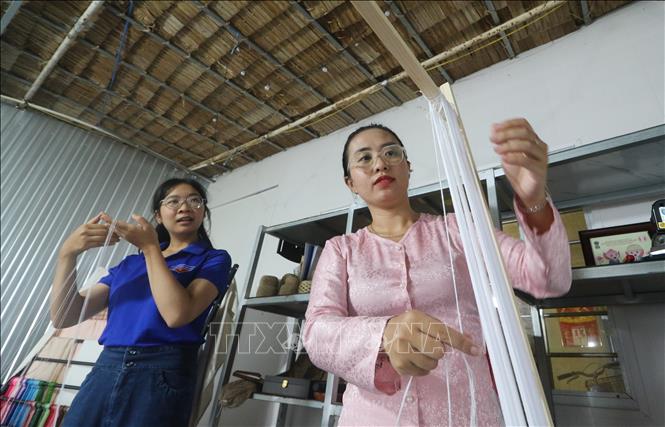Chị Huỳnh Ngọc Như (bên phải) chia sẻ các công đoạn tạo thành sản phẩm từ lụa sen cho các bạn đoàn viên, thanh niên tham quan. Ảnh: Hồng Thái - TTXVN