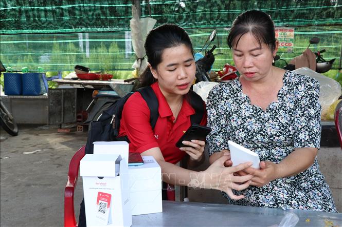 Hướng dẫn tiểu thương chợ Cầu Xây sử dụng bảng mã QR. Ảnh: Thanh Hòa - TTXVN