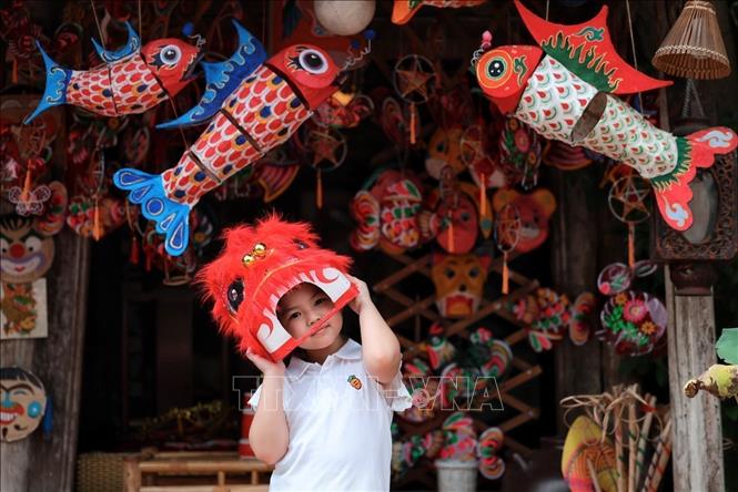 A little girl delights in wearing a lion dance head amidst a vibrant space filled with carp lanterns, traditional masks, and Mid-Autumn toys. VNA Photo: Phạm Tuấn Anh