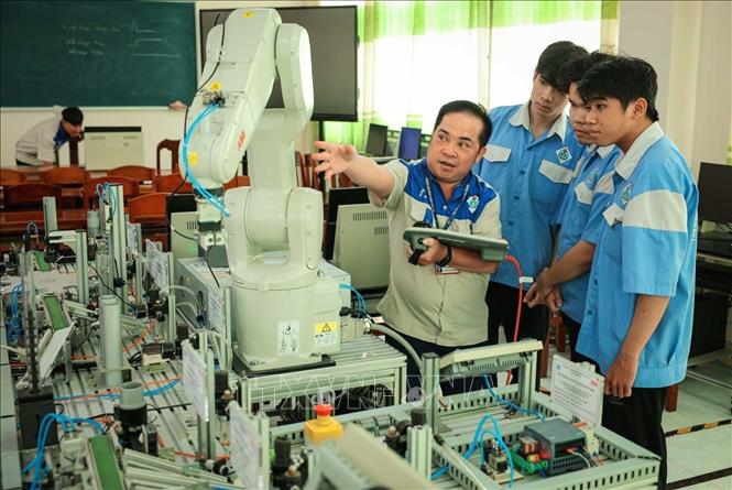 Thạc sĩ Hồ Tấn Đạt - Giảng viên khoa Điện tử hướng dẫn sinh viên nghề Cơ điện tử vận hành Robot lắp ráp sản phẩm. Ảnh: Hoàng Hiếu – TTXVN