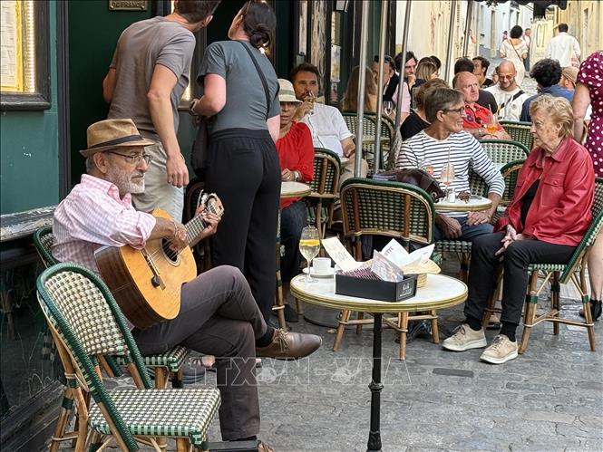 Một nghệ sĩ đường phố chơi đàn guitar giữa không gian quán cà phê ngoài trời trên đồi Montmartre, góp phần tạo nên nét phóng khoáng, nghệ thuật đặc trưng của khu phố. Ảnh: Hữu Chiến - PV TTXVN tại Pháp