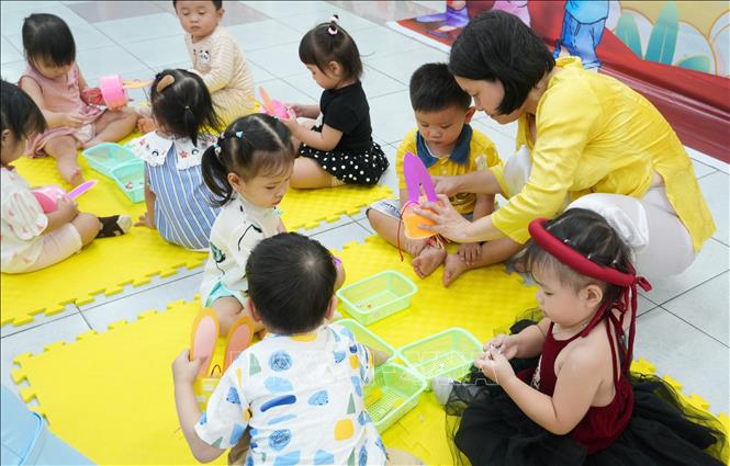 Cô giáo hướng dẫn học sinh mầm non tự trang trí đồ chơi đèn trung thu. Ảnh: Phan Sáu - TTXVN