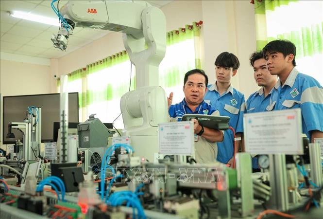 Thạc sĩ Hồ Tấn Đạt – Giảng viên khoa Điện tử hướng dẫn sinh viên điều khiển, làm chủ vận hành cánh tay robot. Ảnh: Hoàng Hiếu – TTXVN