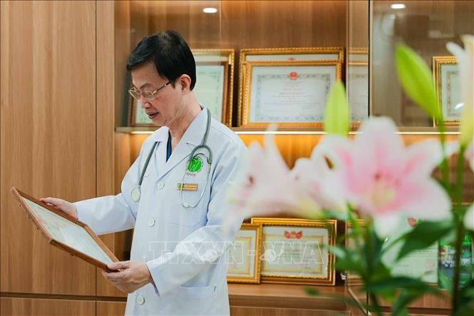 PGS.TS, Thầy thuốc Nhân dân Nguyễn Quang Bình xem lại tấm bằng khen đầu tiên của Khoa Gây mê hồi sức, được Bộ Y tế trao tặng vì thành tích thực hiện nhiệm vụ, kế hoạch y tế năm 2006. Tấm bằng ghi dấu một chặng đường nỗ lực của tập thể khoa, khi đơn vị còn mang tên Viện Răng Hàm Mặt Quốc gia. Ảnh: Phạm Tuấn Anh - TTXVN