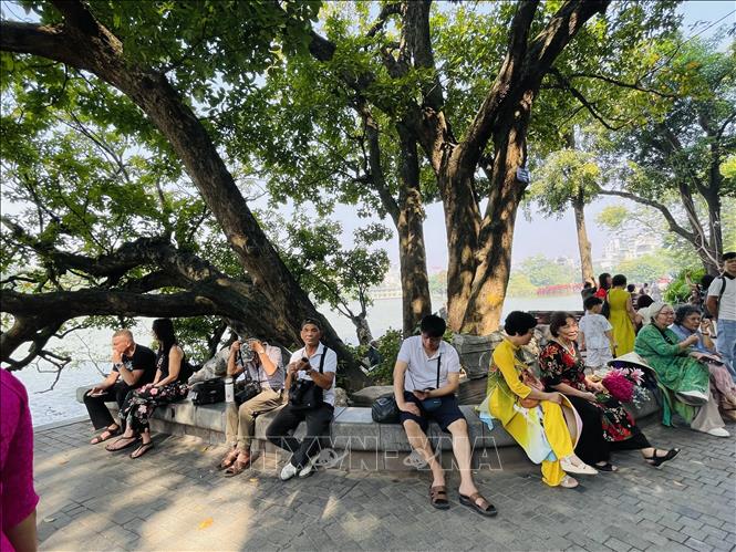 Người dân và du khách nghỉ chận bên gốc cây cổ thụ ven hồ Hoàn Kiếm để cảm nhận không khí dễ chịu của mùa Thu Hà Nội. Ảnh: Tuyết Mai - TTXVN