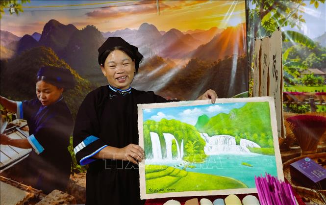Chị Nông Thị Kính (xóm Rìa Trên, xã Quảng Uyên) với sản phẩm bức tranh vẽ trên giấy bản truyền thống. Ảnh: Chu Hiệu-TTXVN.