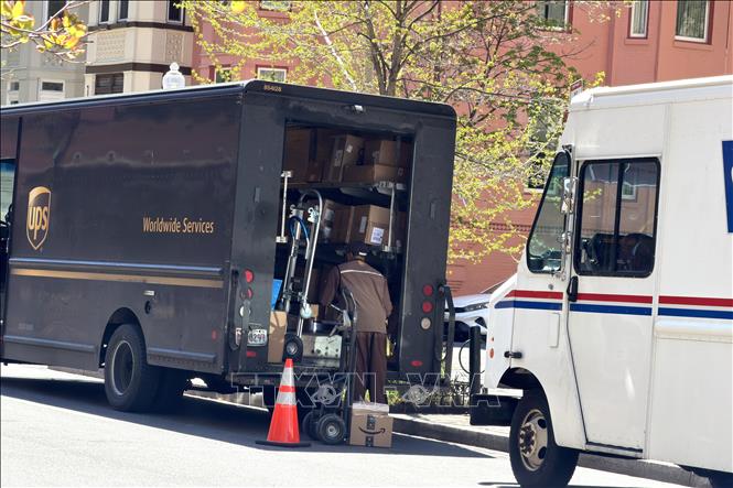 Nhân viên Công ty chuyển phát nhanh UPS (United Parcel Service) chuẩn bị bưu phẩm để giao cho khách hàng trên một tuyến phố ở Washington, D.C.; phía sau là xe của Bưu chính Mỹ (USPS). Ảnh: Ngọc Quang – PV TTXVN tại Mỹ
