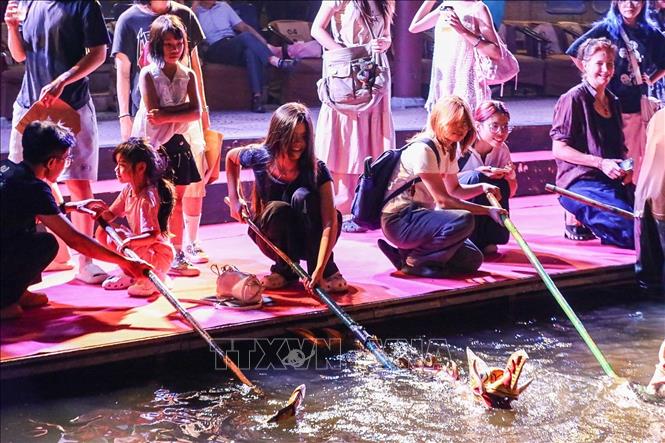 Khán giả trải nghiệm trực tiếp điều khiển con rối dưới sự hướng dẫn của các nghệ nhân múa rối nước. Ảnh: Khánh Hoà - TTXVN