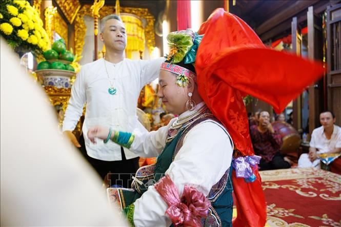 Người phụ lễ hỗ trợ thanh đồng trong quá trình thay đổi, điều chỉnh trang phục khi thực hành nghi lễ hầu đồng tại đền Hàng Vải. Bên cạnh thanh đồng và các cung văn, những người phụ lễ giữ vai trò hỗ trợ chuẩn bị khăn áo, vật phẩm và phối hợp thực hiện các công đoạn nghi lễ. Sự tham gia của nhiều thành viên thể hiện tính cộng đồng trong thực hành tín ngưỡng, nơi những kiến thức và kỹ năng truyền thống được duy trì thông qua hoạt động thực hành. Ảnh: Phạm Tuấn Anh - TTXVN