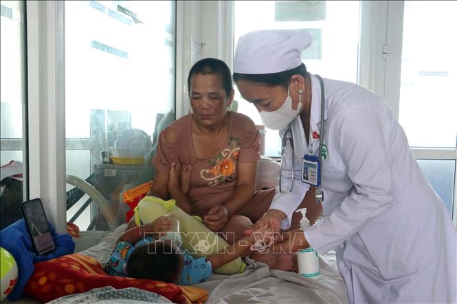 Bác sĩ kiểm tra các triệu chứng trên cơ thể của một bệnh nhi đang điều trị bệnh tay chân miệng. Ảnh: Trung Kiên - TTXVN
