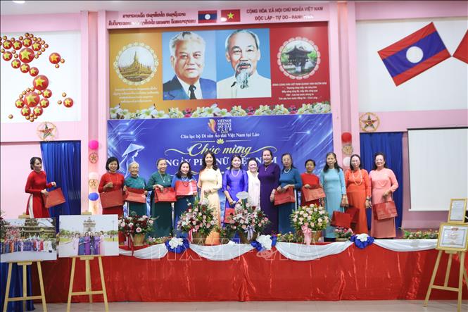 Bà Vũ Thị Dung, Phu nhân Đại sứ Việt Nam tại Lào và bà Biện Thị Kỷ trao tặng áo dài cho các nữ thành viên Hội Cựu lưu học sinh Lào từng học tập tại Việt Nam. Ảnh: Xuân Tú – PV TTXVN tại Lào