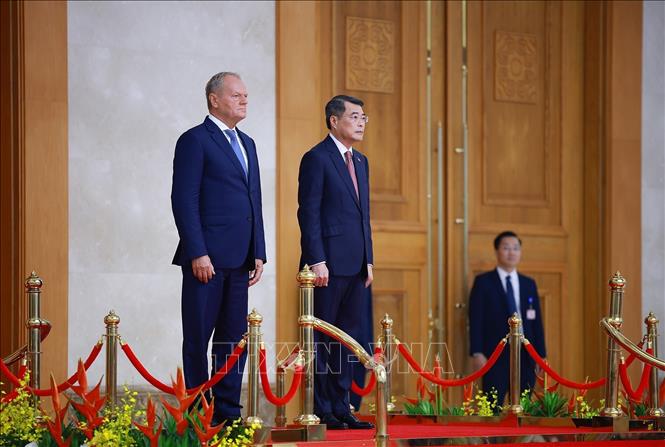 Thủ tướng Lê Minh Hưng và Thủ tướng Ba Lan Donald Tusk thực hiện nghi lễ chào cờ. Ảnh: Dương Giang – TTXVN 
