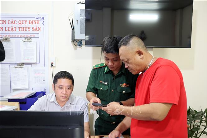 Cán bộ Biên phòng hỗ trợ ngư dân cài đặt, sử dụng phần mềm eCDT (hệ thống phần mềm truy xuất nguồn gốc thủy sản khai thác điện tử) tại cảng cá INCOMAP. Ảnh: Đoàn Mạnh Dương-TTXVN